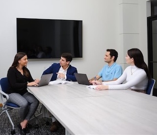 Graduate students sitting around a table having a discussion in professional attire.